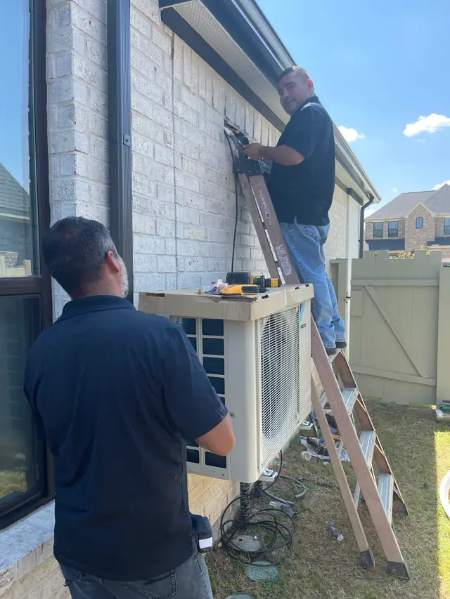Two technicians installing a ductless condenser